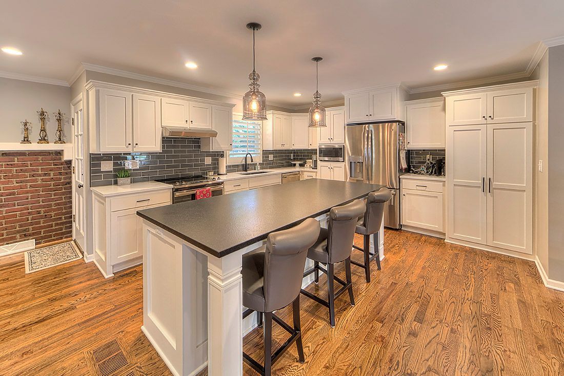 A kitchen with white cabinets , stainless steel appliances , a large island , and hardwood floors.