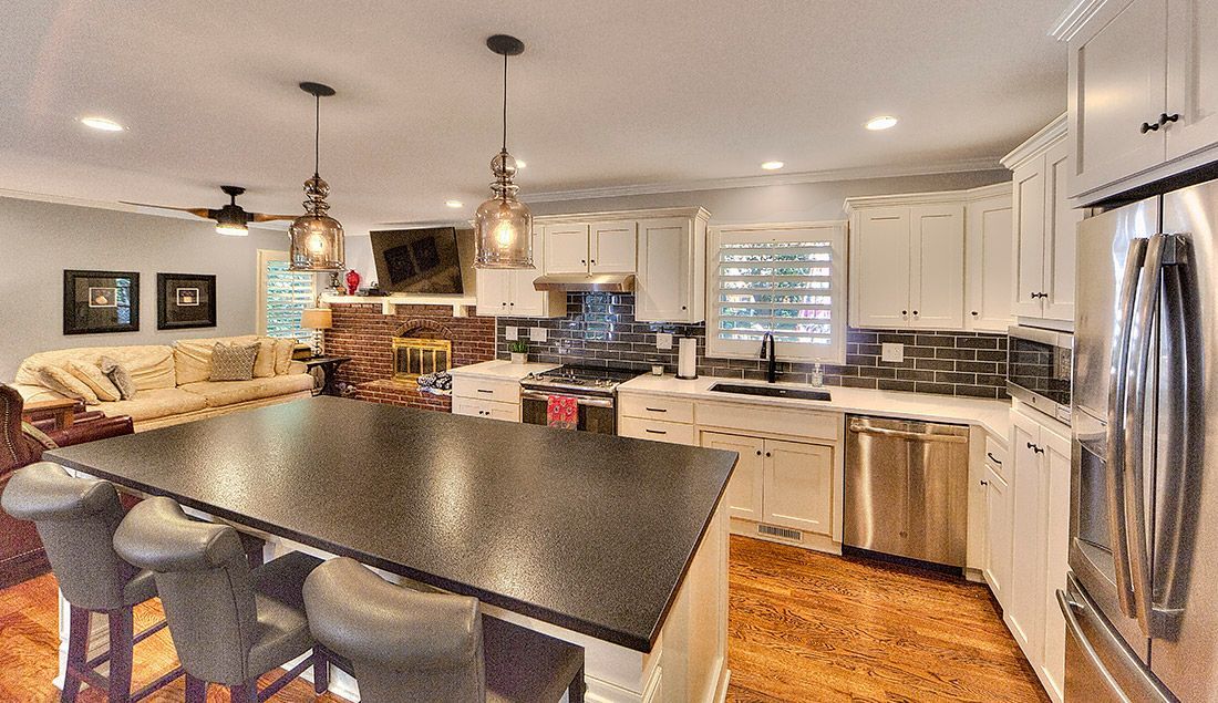 A kitchen with white cabinets , stainless steel appliances , a black counter top and a large island.