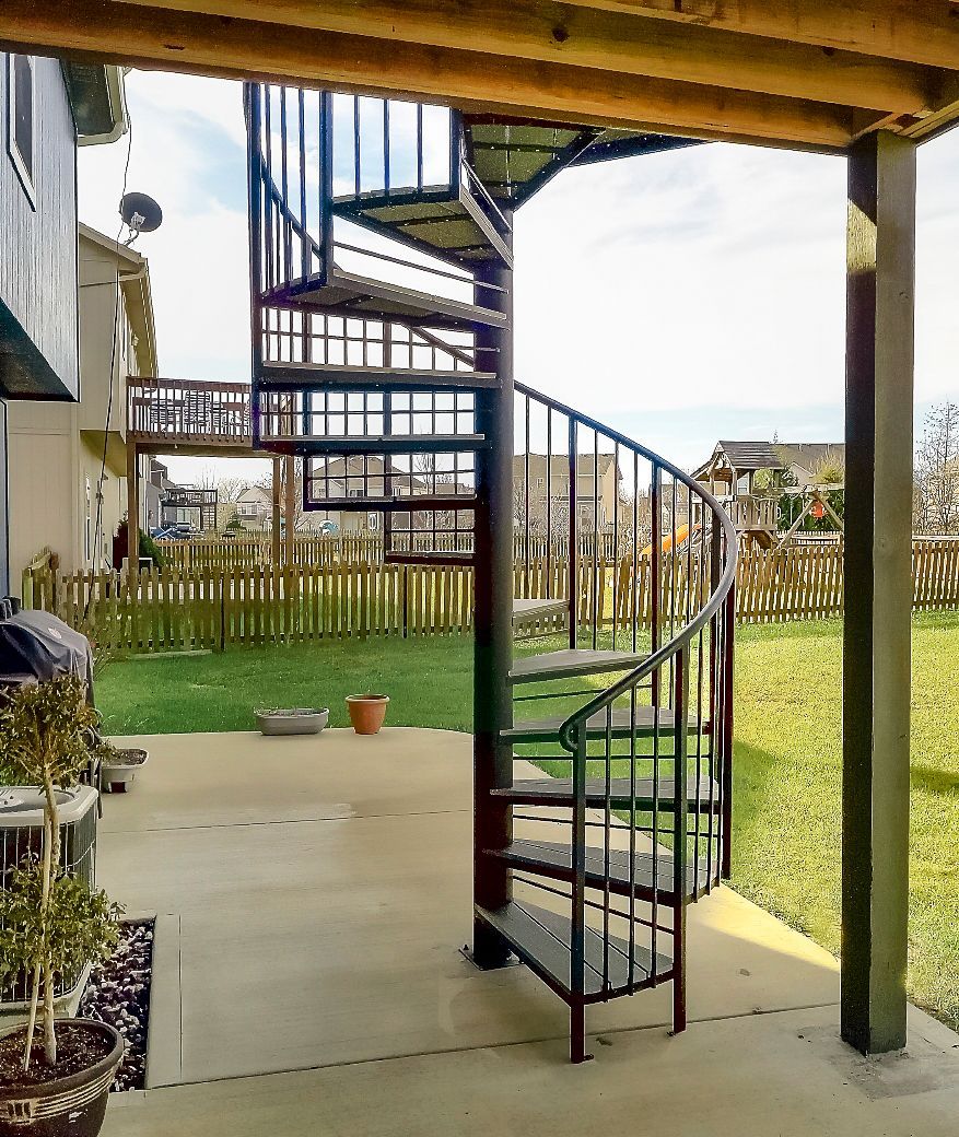 A spiral staircase is sitting on a patio next to a house.
