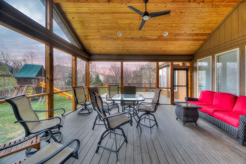 A screened in porch with a table and chairs and a ceiling fan.