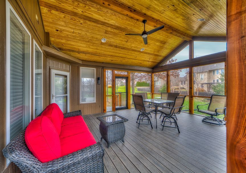 A screened in porch with a table and chairs and a ceiling fan.