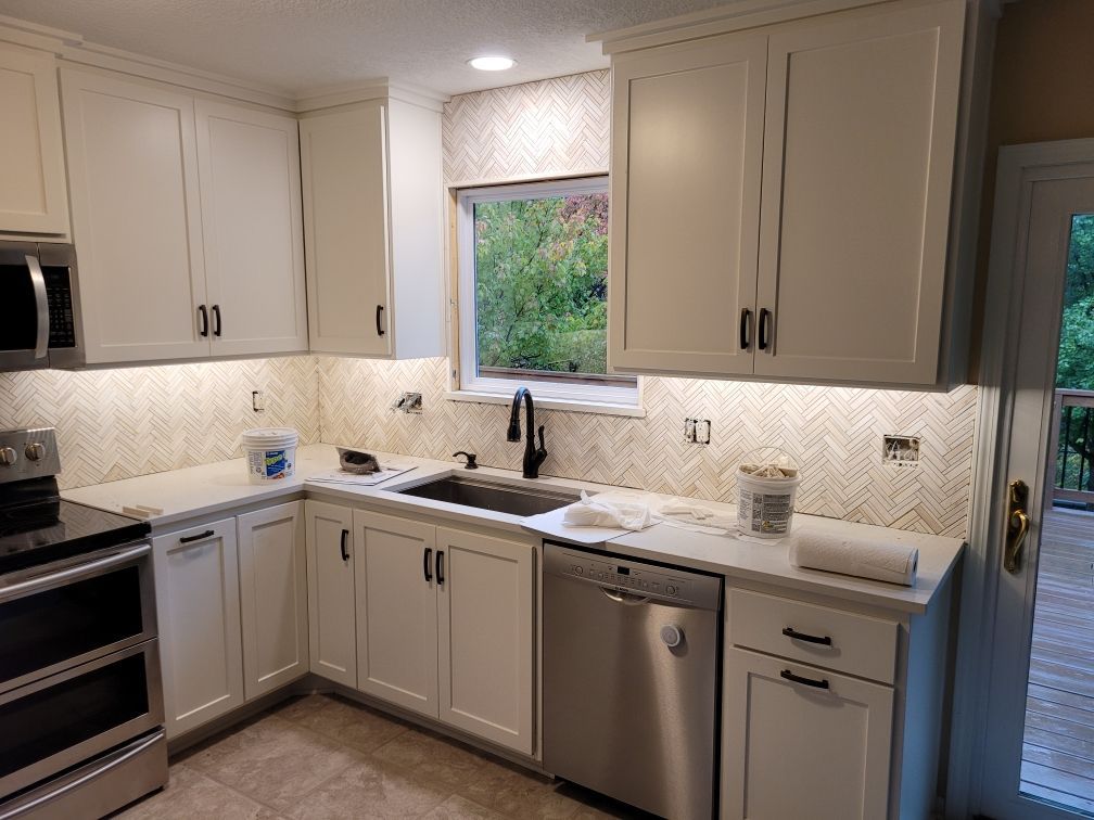 A kitchen with white cabinets , stainless steel appliances , a sink , and a window.