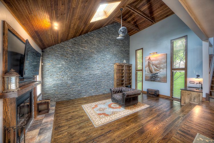 A living room with hardwood floors , a stone wall , a fireplace and a flat screen tv.