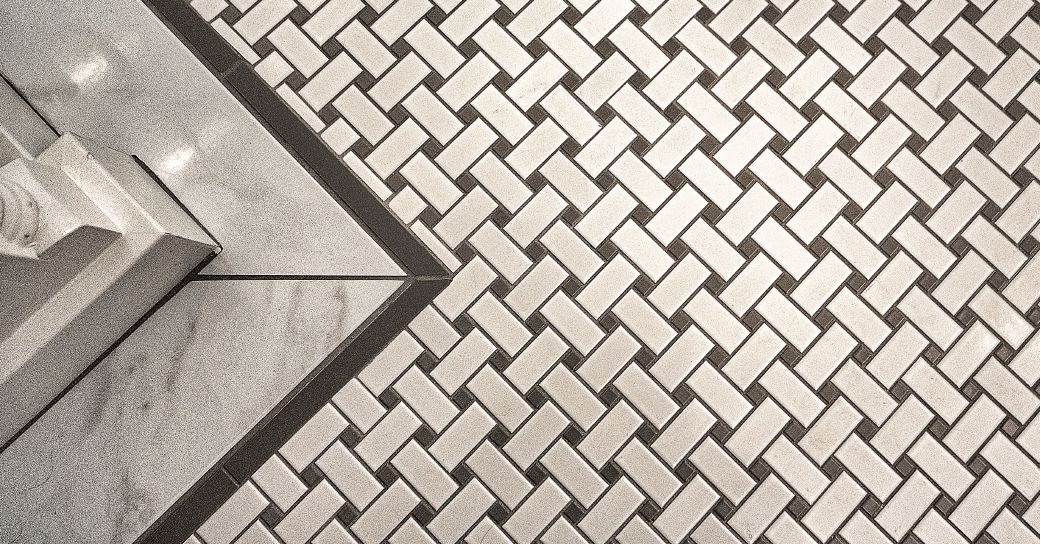 A black and white photo of a tile floor with a herringbone pattern.