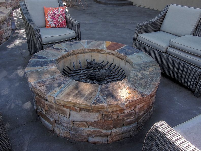 A fire pit is surrounded by chairs and a couch on a patio.