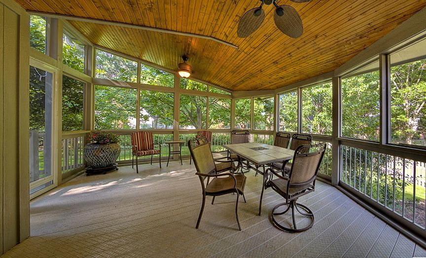 A screened in porch with a table and chairs and a ceiling fan.
