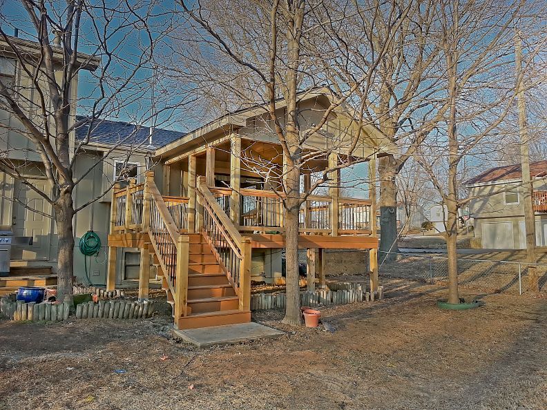 A small wooden house with stairs leading up to it is surrounded by trees.