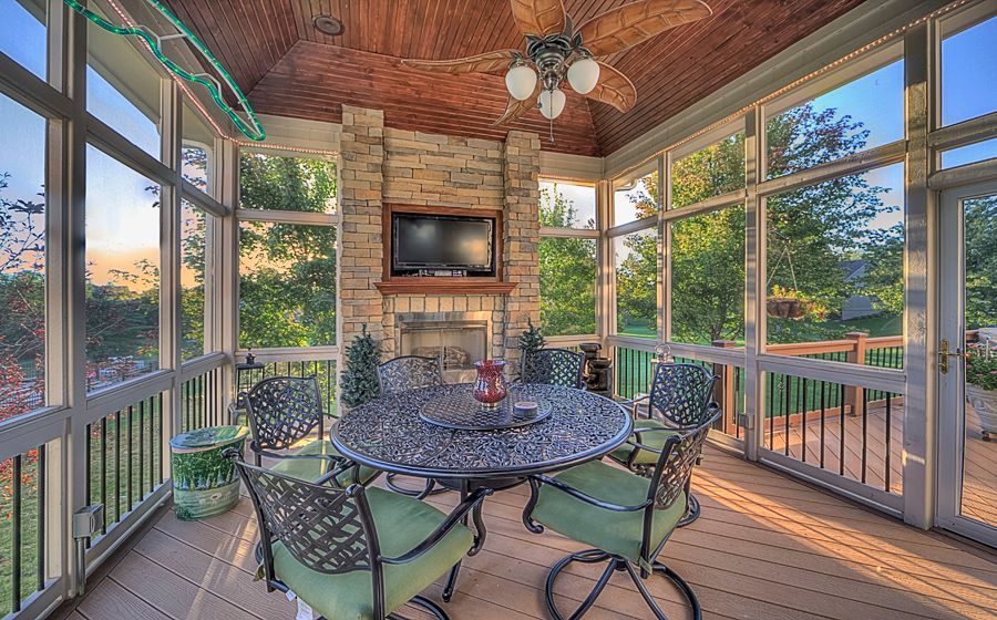 A screened in porch with a table and chairs and a television.