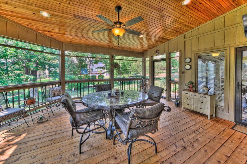 A screened in porch with a table and chairs and a ceiling fan.