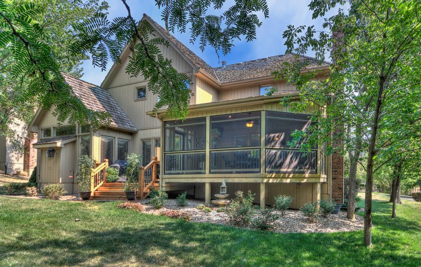 A house with a screened in porch is surrounded by trees.