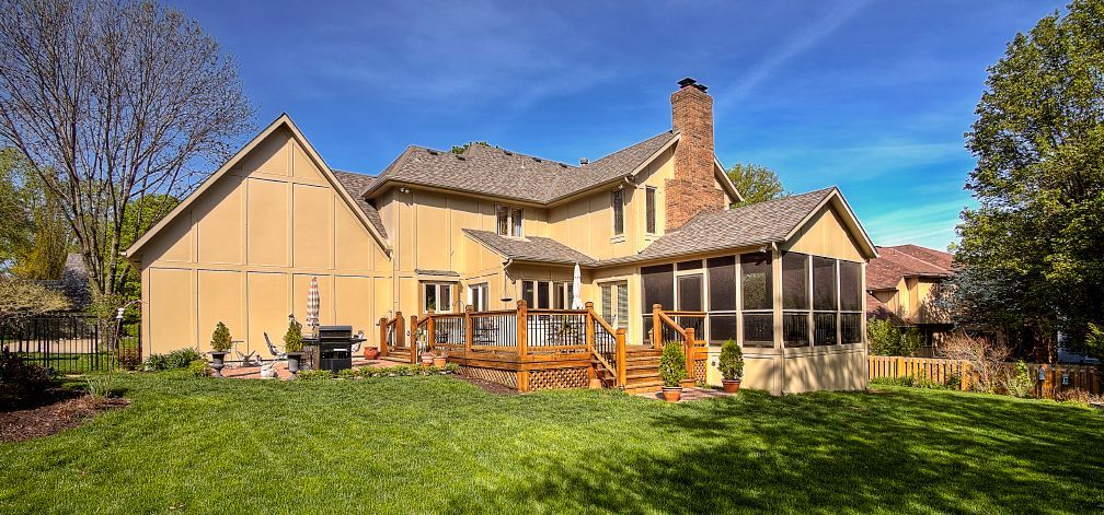 A large house with a screened in porch and a large lawn in front of it.