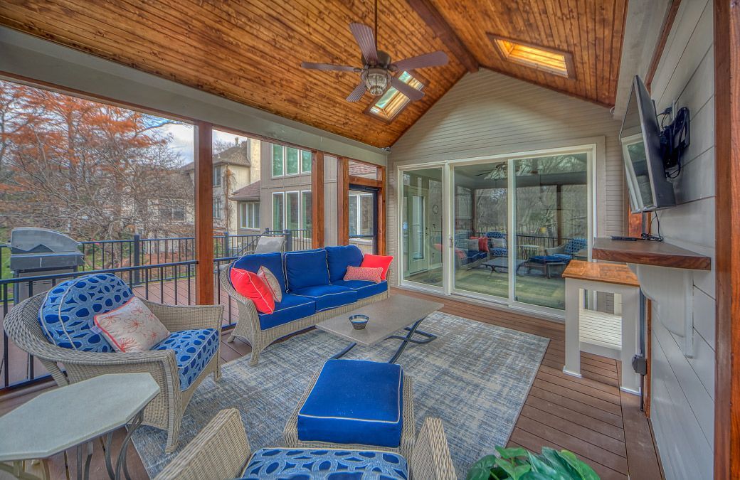 A screened in porch with a couch , chairs , and a television.