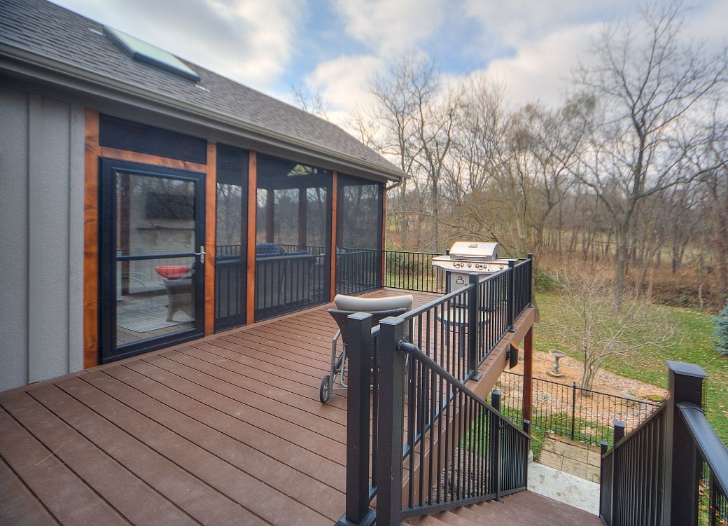 A large deck with a screened in porch and stairs leading up to it.