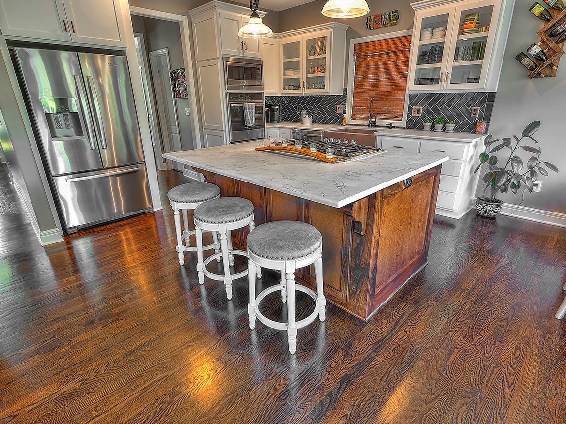 A kitchen with a large island , stools and a refrigerator.