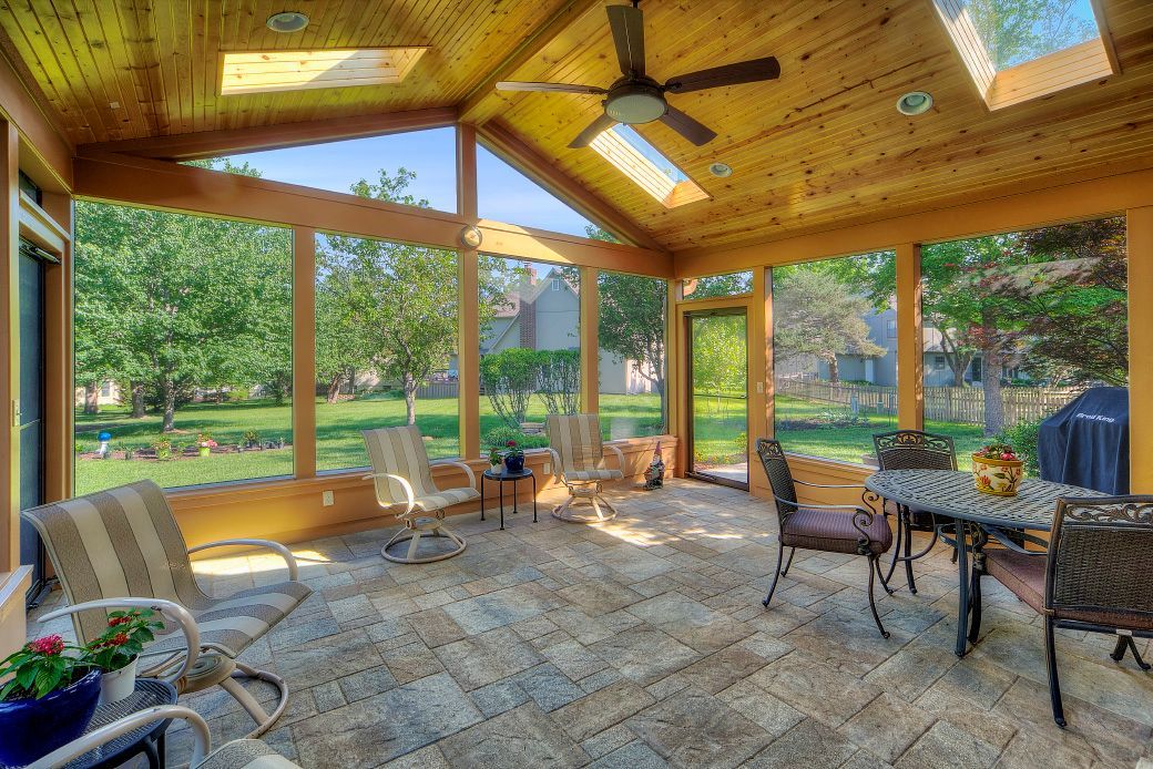 A screened in porch with a table and chairs and a ceiling fan.