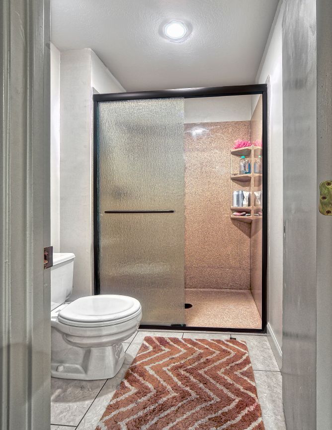 A bathroom with a toilet , shower and rug.