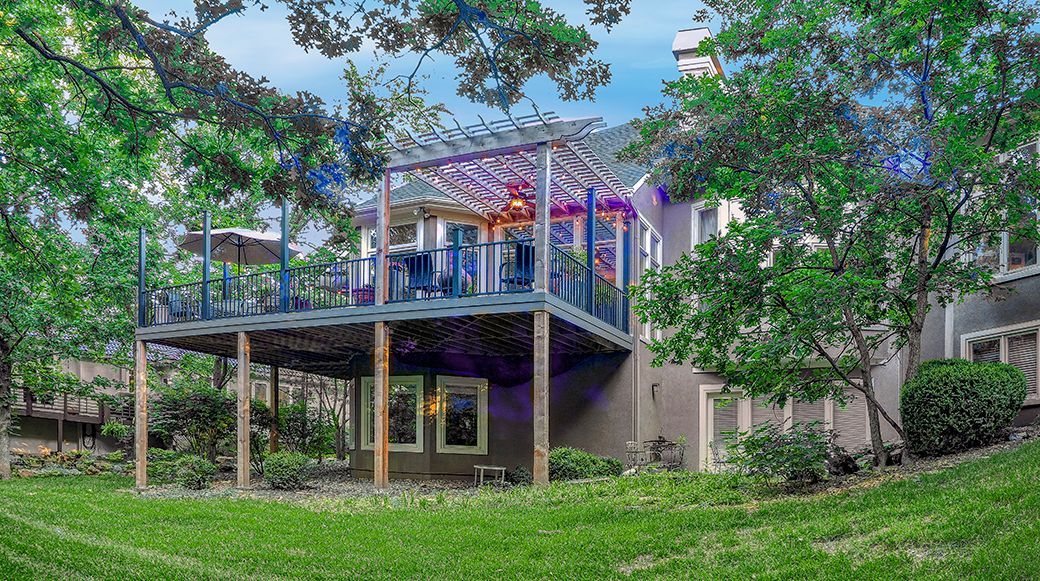 The back of a house with a large deck surrounded by trees.