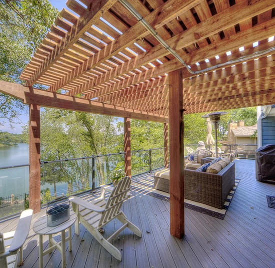 A wooden deck with a pergola overlooking a lake