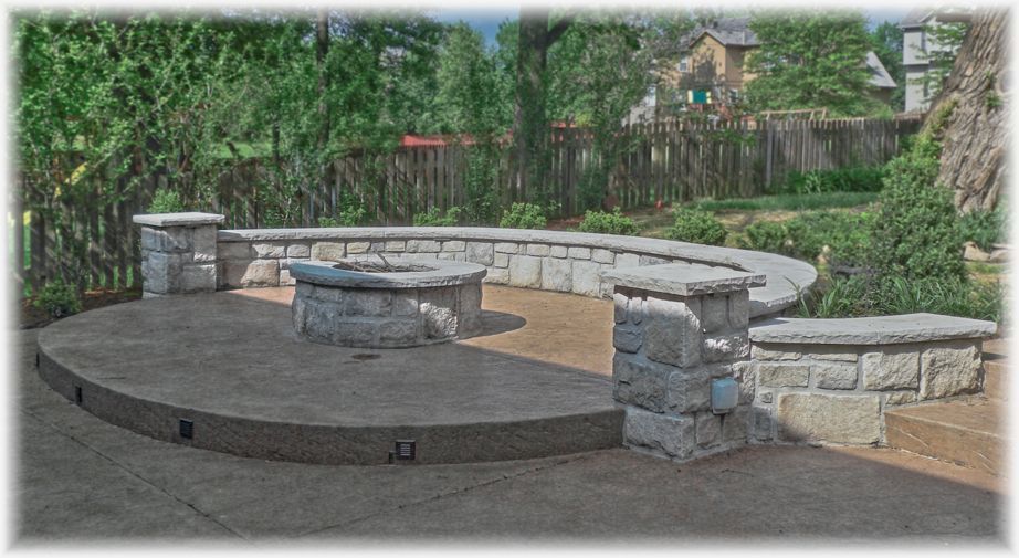 A concrete patio with stone benches and a fire pit