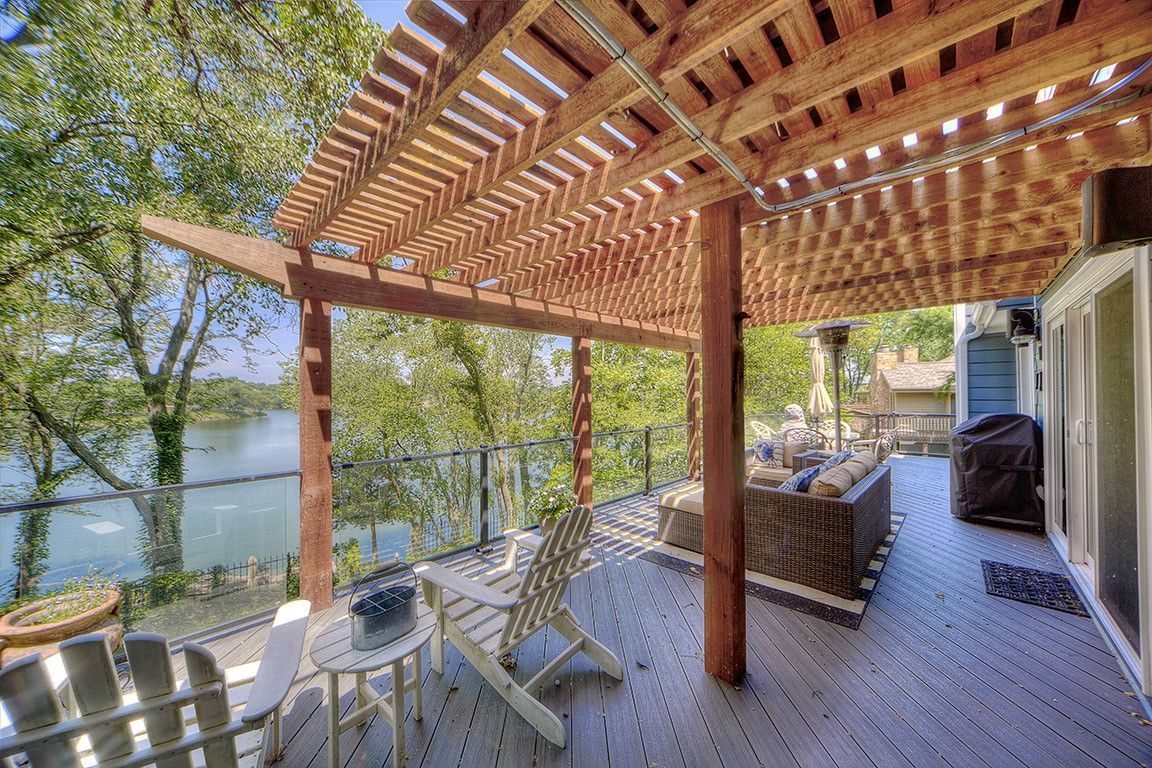 A wooden deck with a pergola overlooking a lake.
