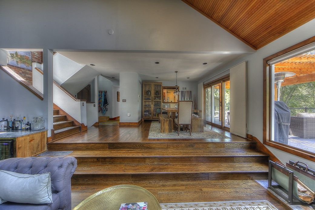 A living room with hardwood floors , stairs , a couch , and a large window.