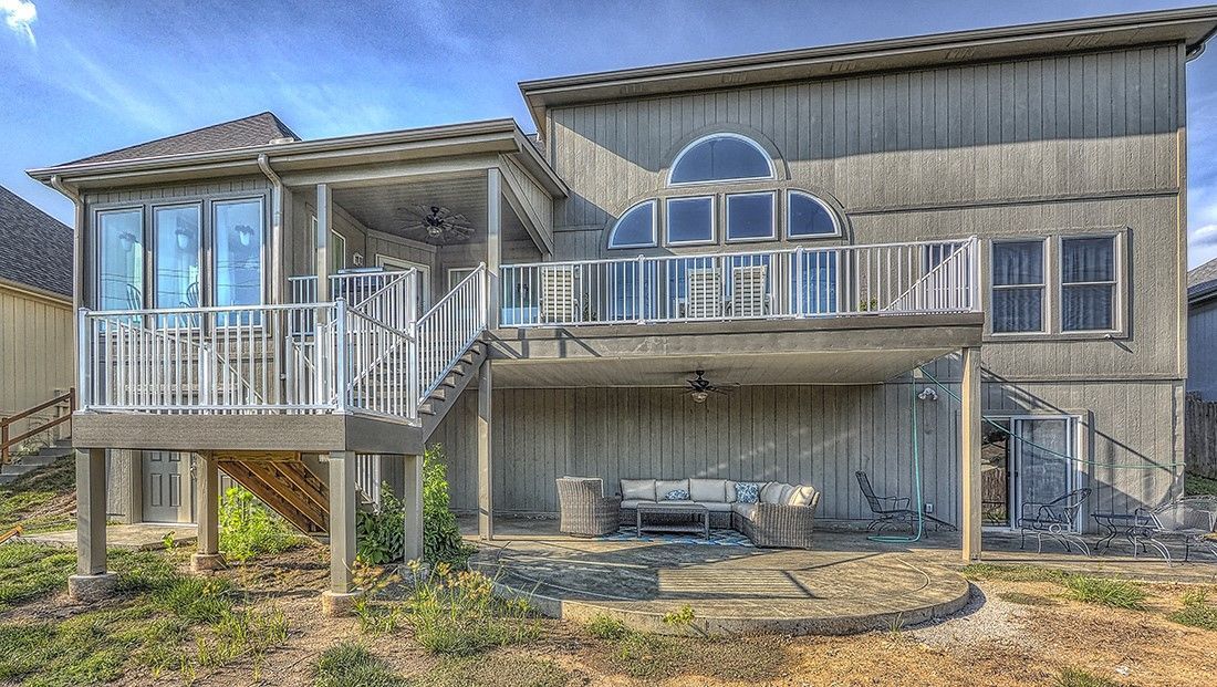 The back of a large house with a large deck and stairs leading up to it.