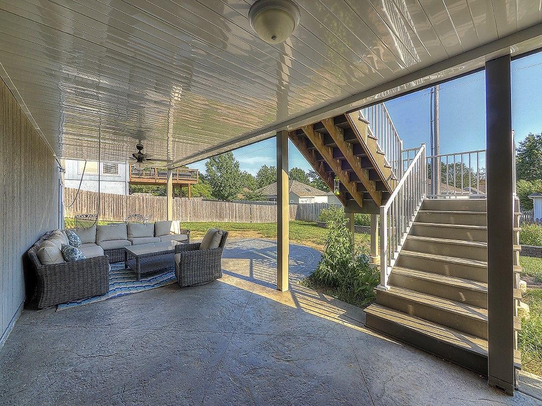 A porch with a couch , chairs , and stairs leading to a deck.