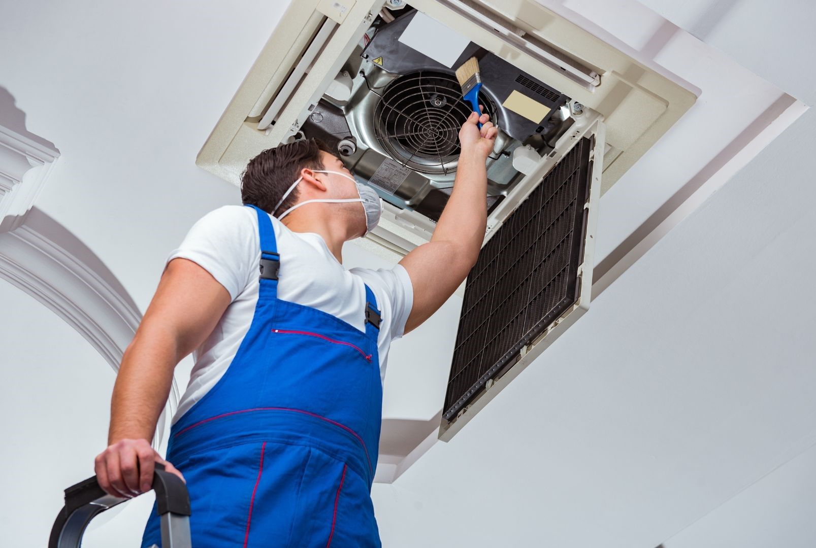 A man wearing a mask is working on an air conditioner.