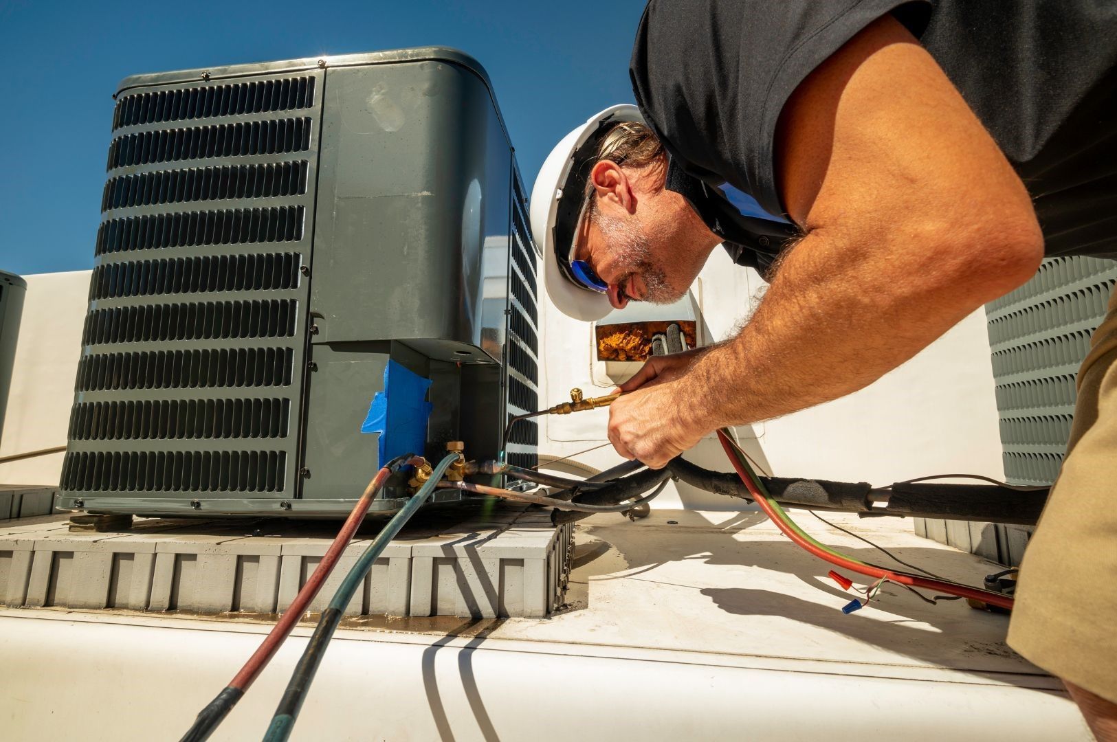 A man is working on an air conditioner on the roof of a building.