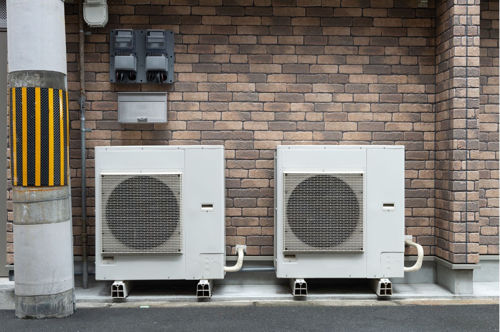 Two air conditioners are sitting outside of a brick building.