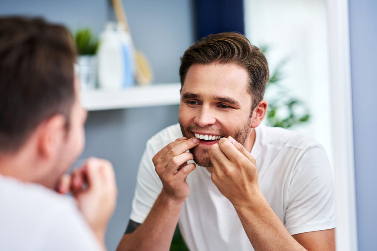 A man is flossing his teeth in front of a mirror.