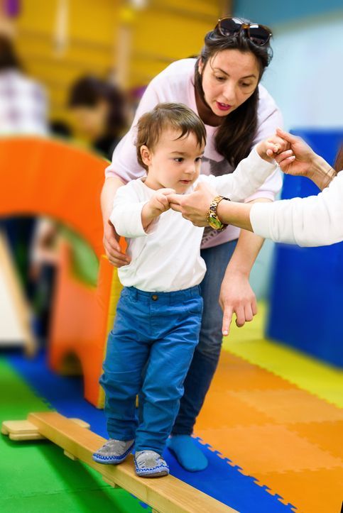 Mother assisting child walking on beam with teacher