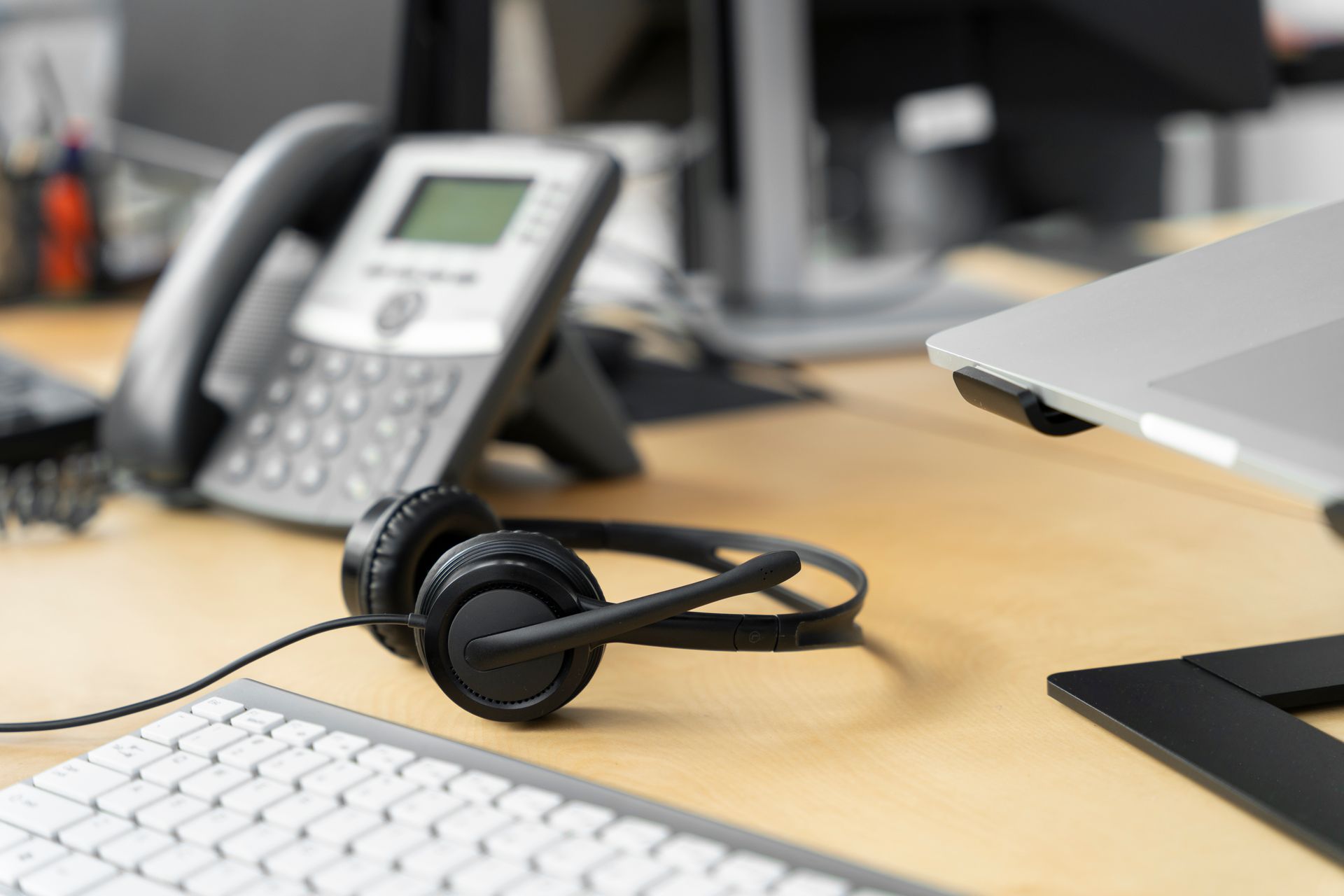 A headset is sitting on a desk next to a laptop and a phone.