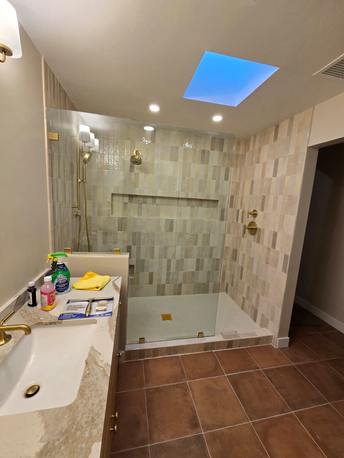 A bathroom with a walk in shower , sink , and skylight.