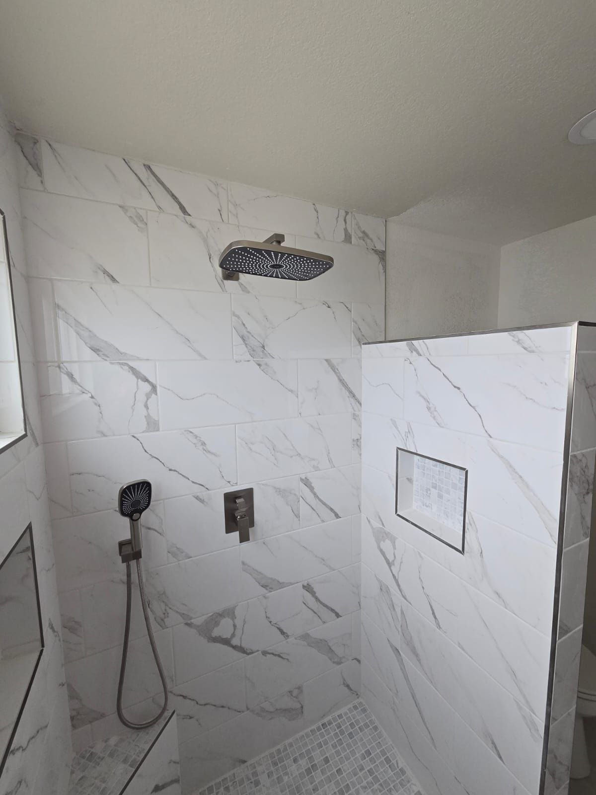 A bathroom with marble tiles and a walk in shower with a shower head.
