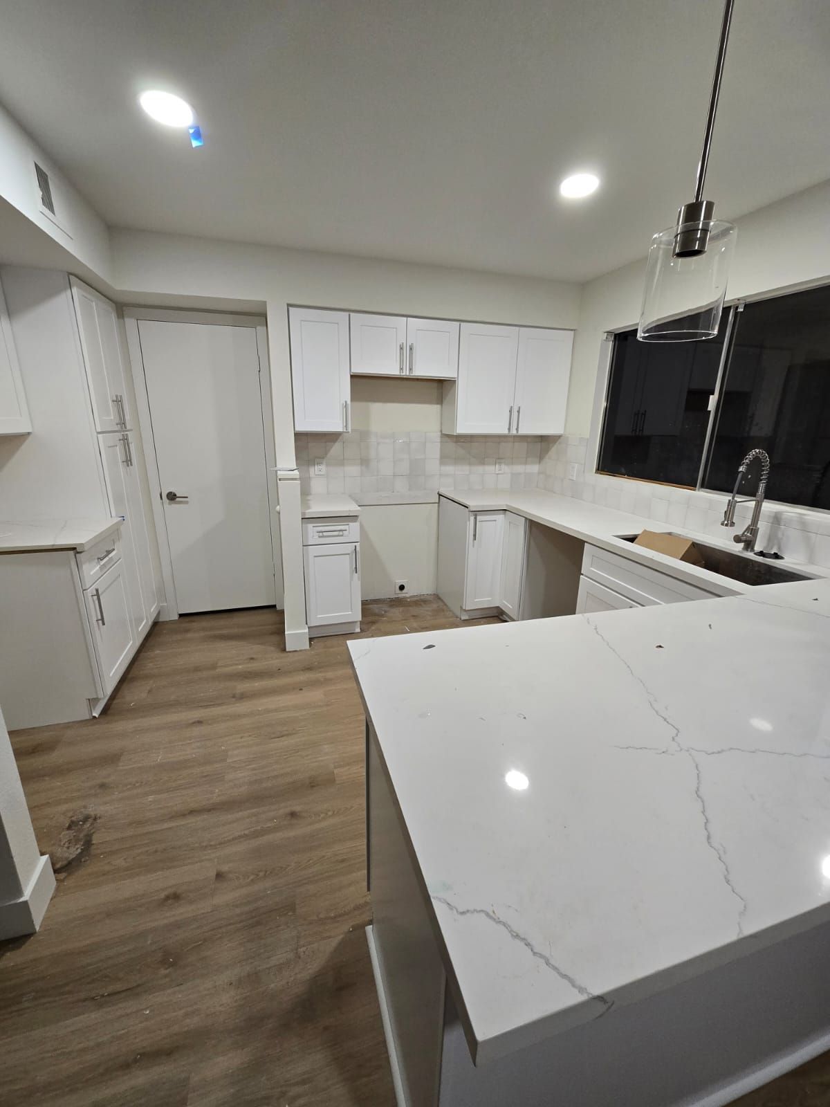 A kitchen with white cabinets , white counter tops , a sink and a window.