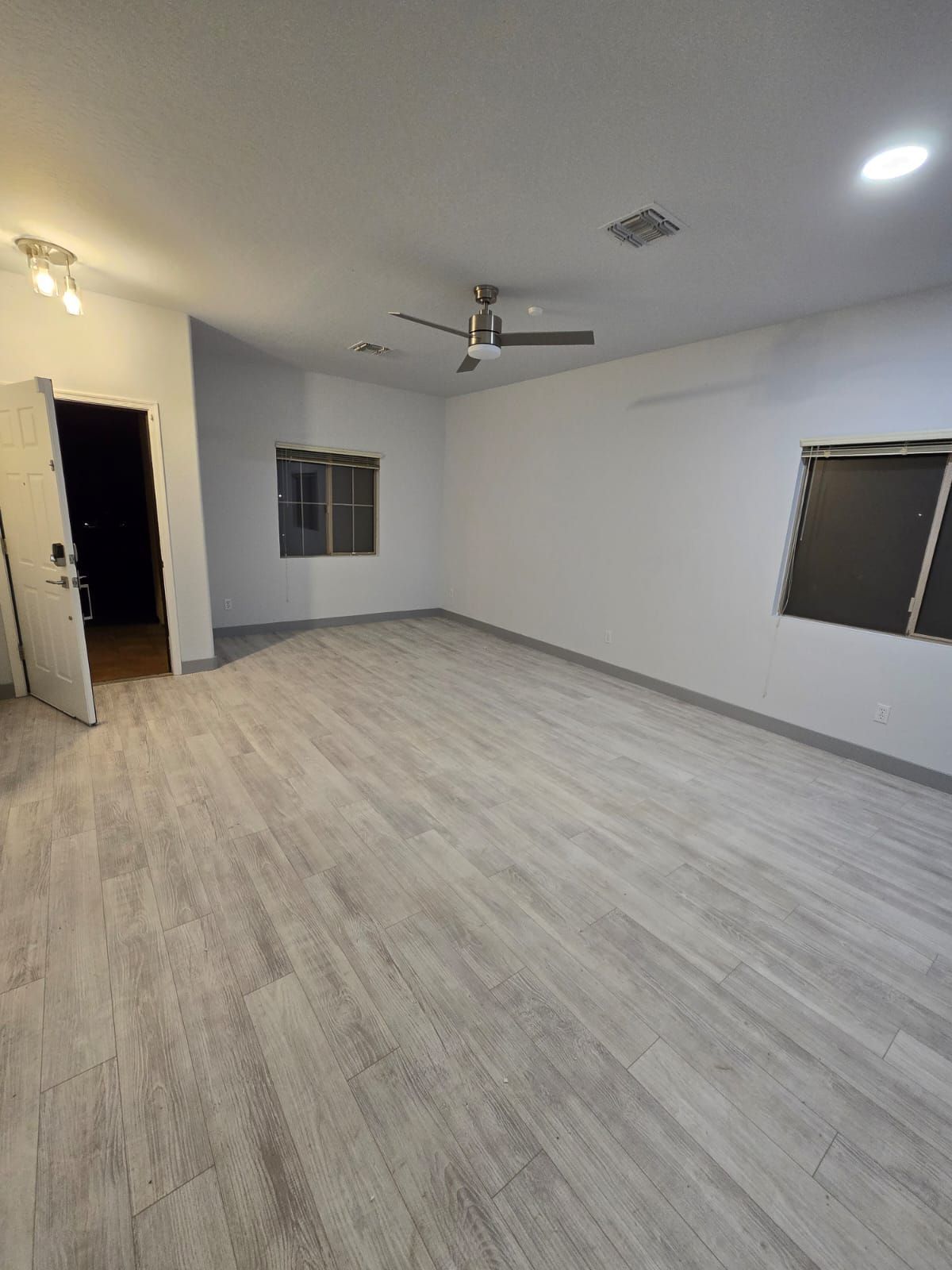 A large empty room with a ceiling fan and two windows.