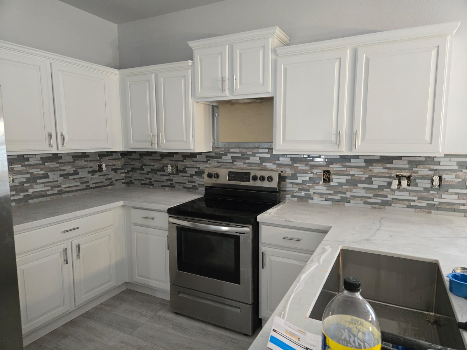 A kitchen with white cabinets , a stove , and a sink.