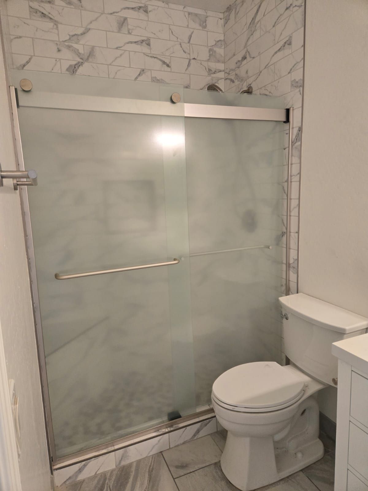 A bathroom with a toilet , shower and sliding glass door.