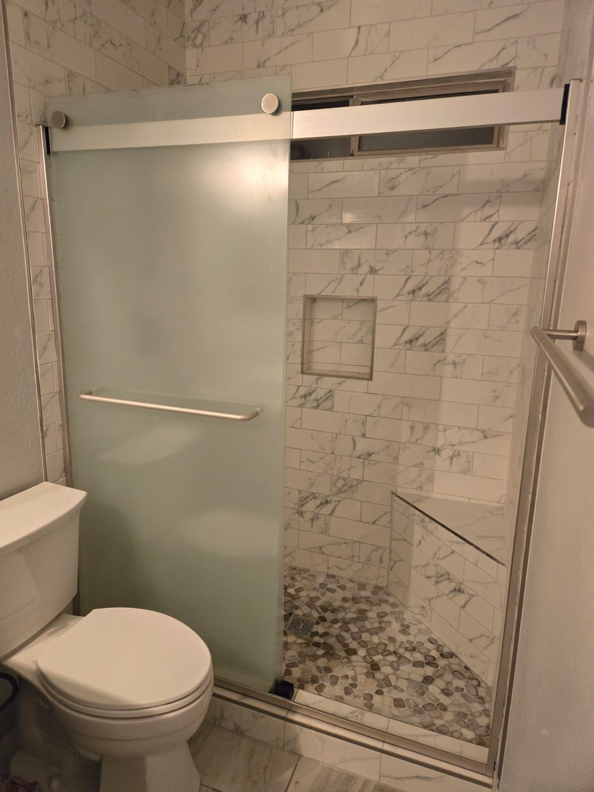 A bathroom with a toilet , shower and sliding glass door.