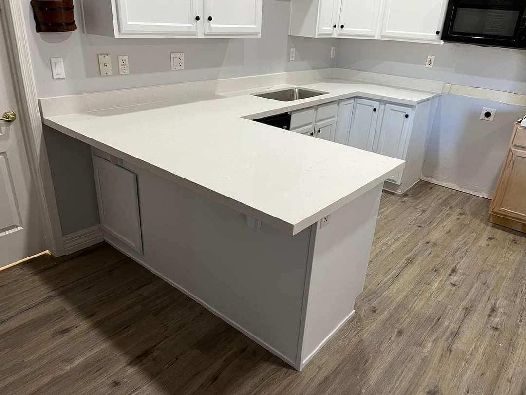 A kitchen with white cabinets , white counter tops , a sink and a microwave.