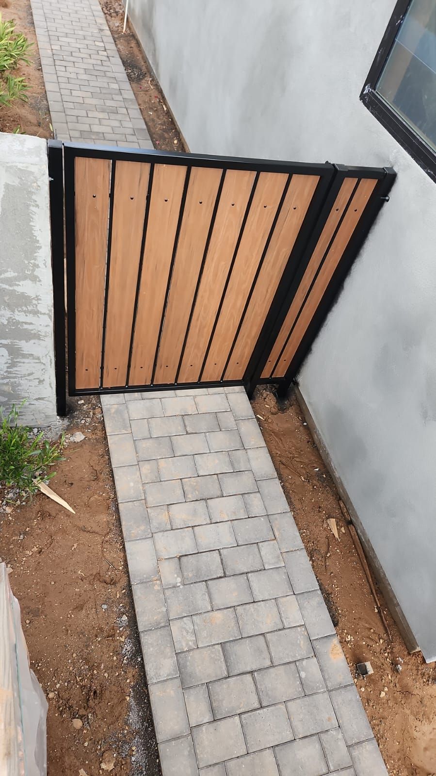 A wooden gate is sitting on the side of a brick walkway.