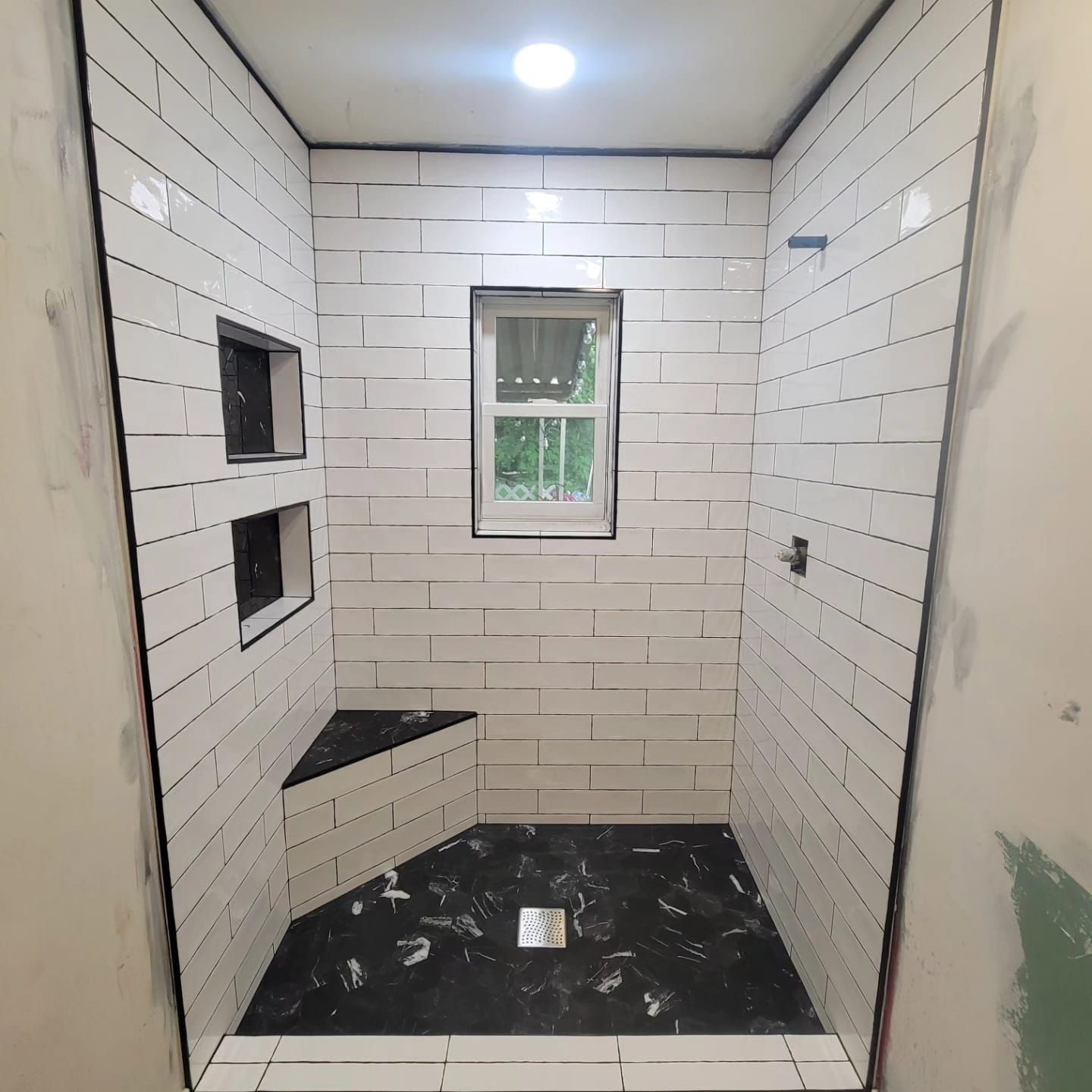 A shower stall with white tiles and a window.