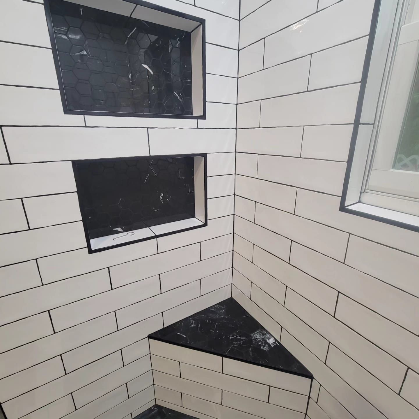 A bathroom with white tiles and black marble shelves and a window.