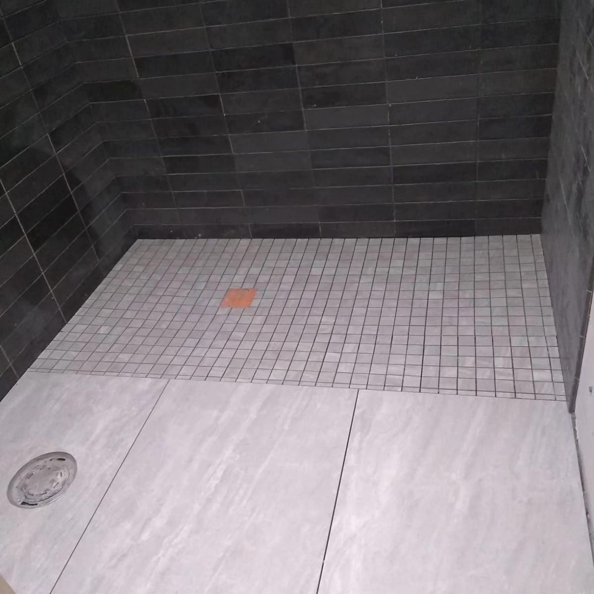 A bathroom with a tiled floor and black tiles on the walls.