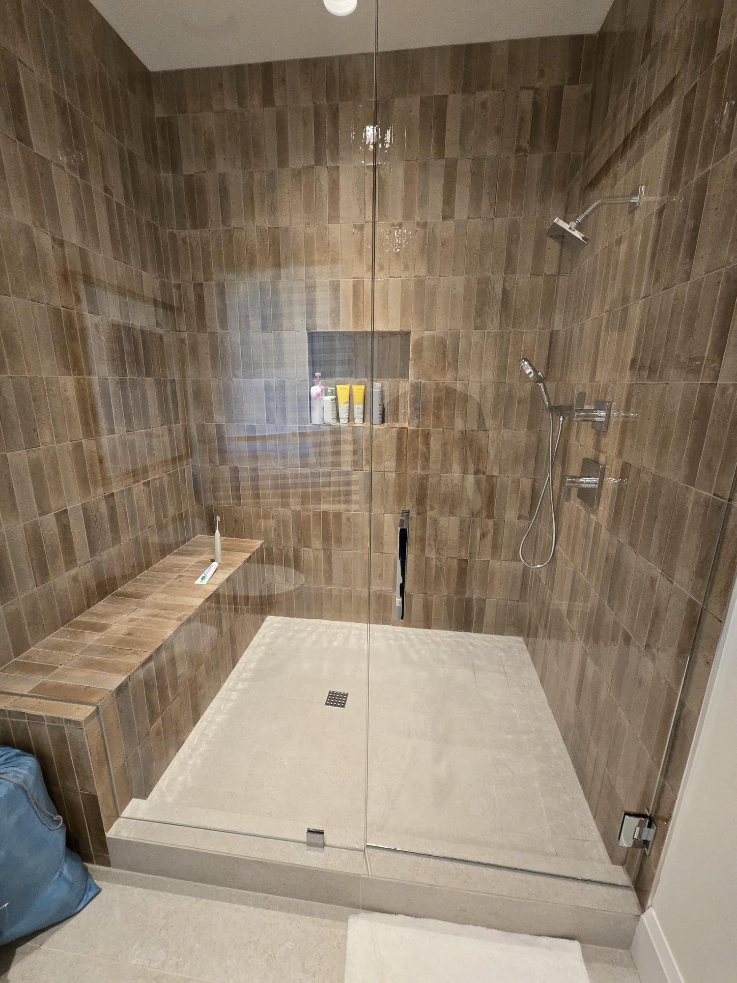 A bathroom with a walk in shower with a glass door and a bench.