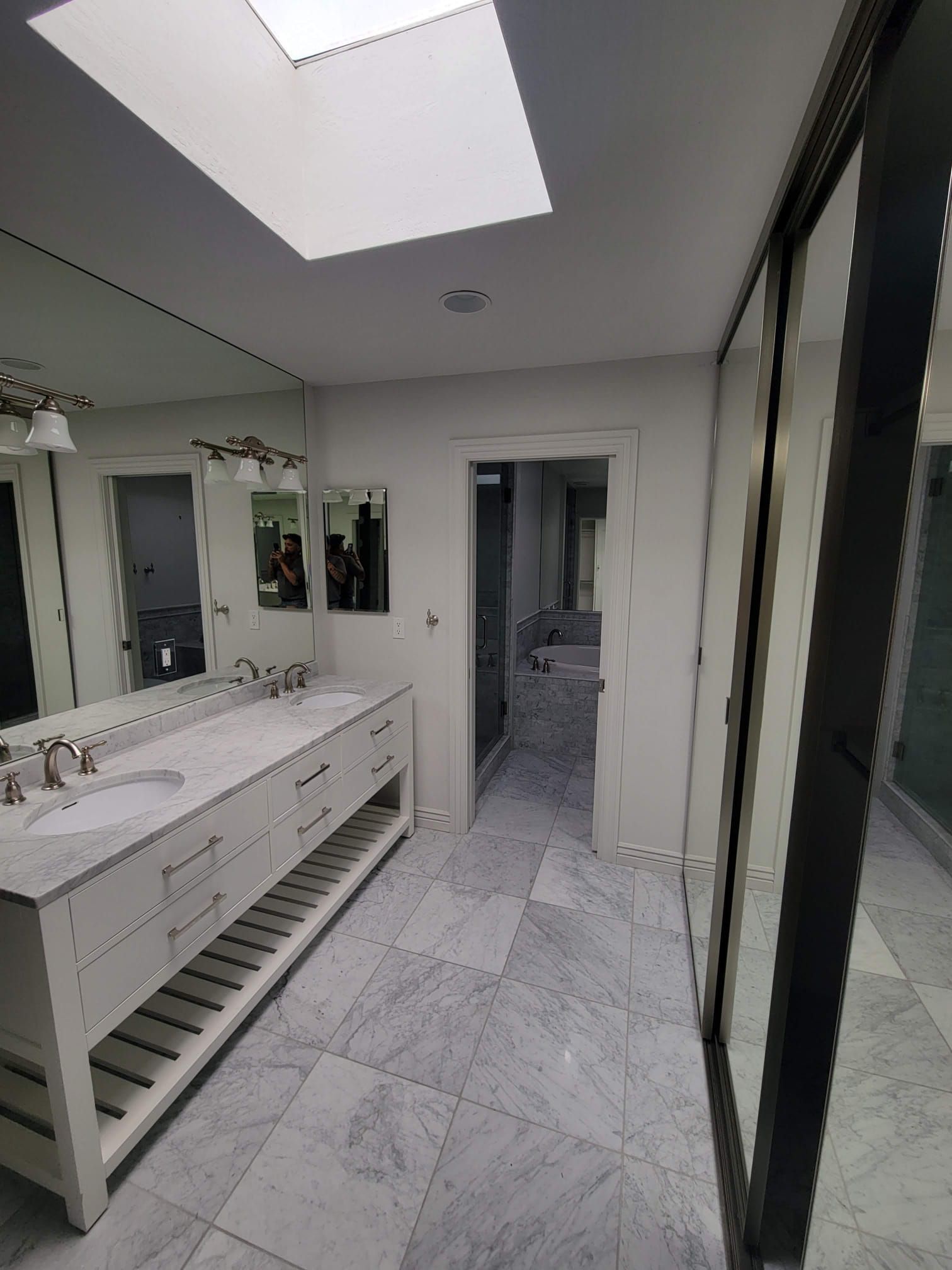 A bathroom with two sinks , mirrors and a skylight.