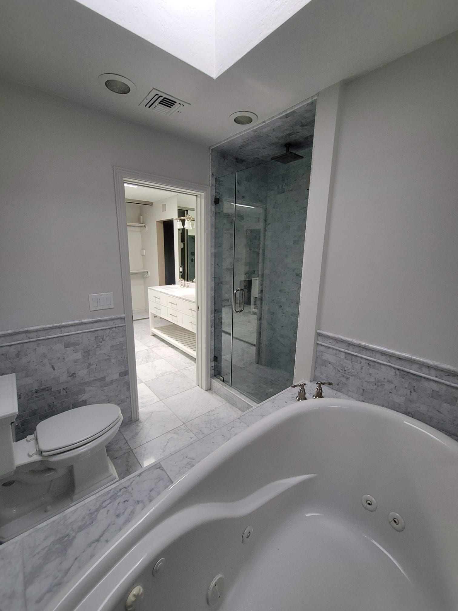 A bathroom with a tub , toilet , shower and skylight.
