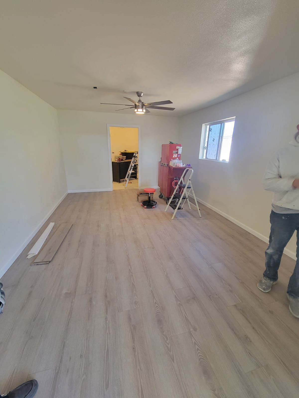 A man is standing in a room with a ladder and a ceiling fan.