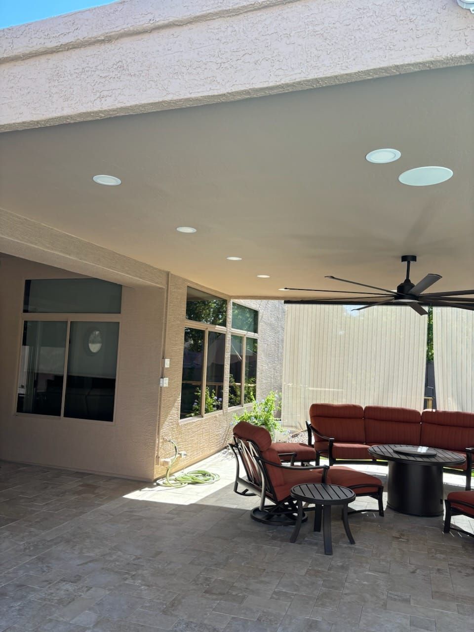 A patio with a couch , chairs , a table and a ceiling fan.